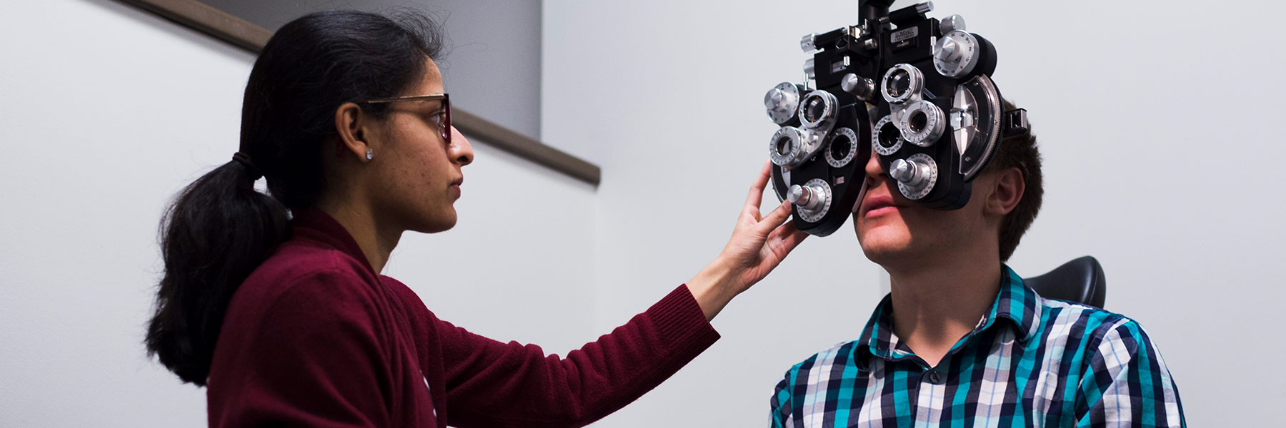 An optometrist student positions equipment in front of a patient's eyes