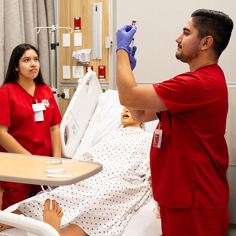 Two students work in the sim lab with a dummy patient