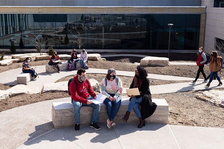 Students sit on limestone rock benches along winding courtyard paths