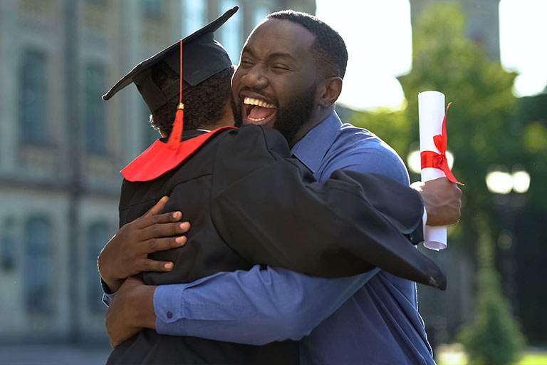 Man hugging graduate in commencement cap and gown
