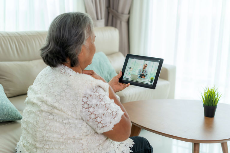 A woman sitting in living room chair looks at doctor through tablet screen